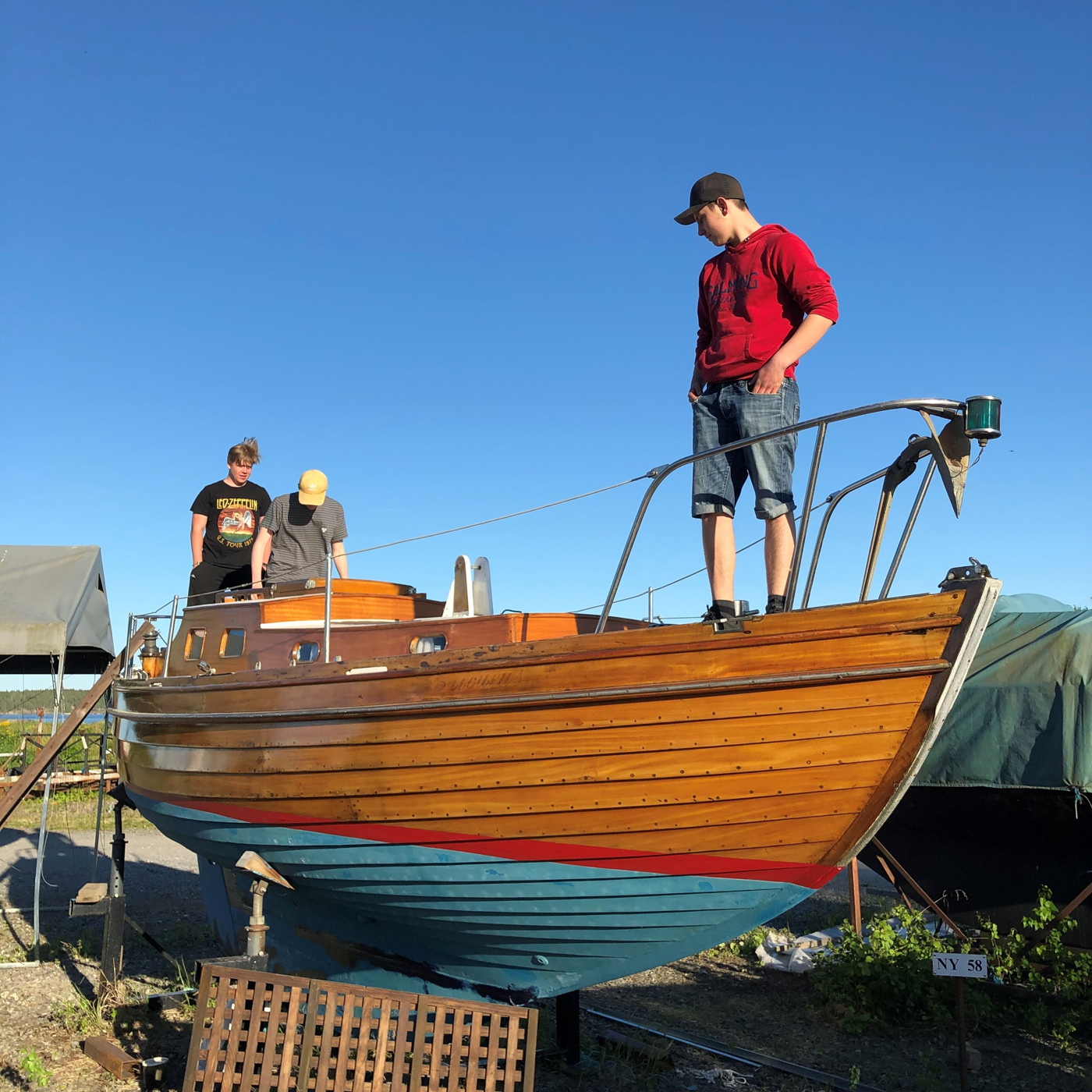 Tre killar står på en båt på land