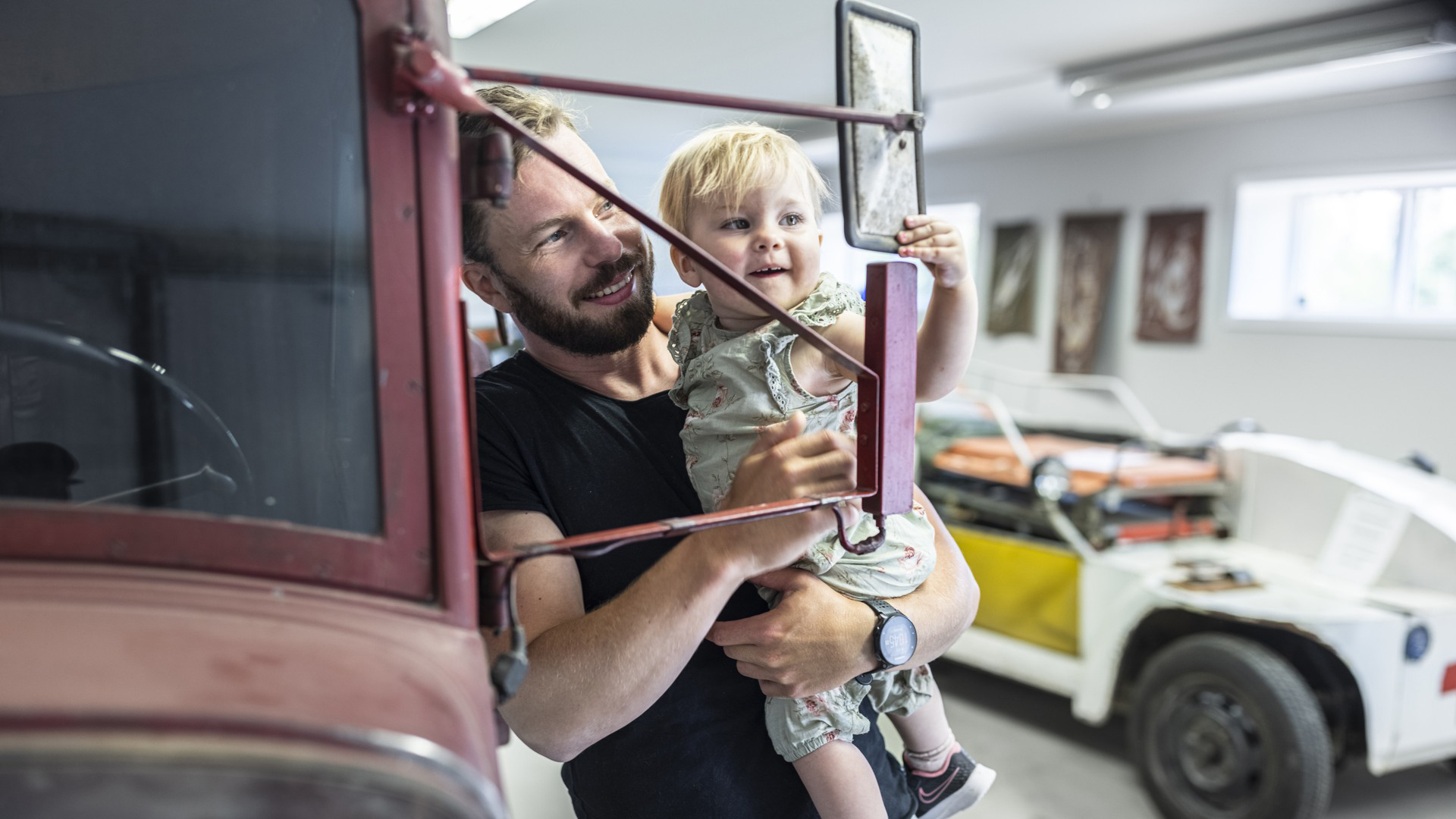 Pappa med barn tittar i spegel på gammal bil på muséet
