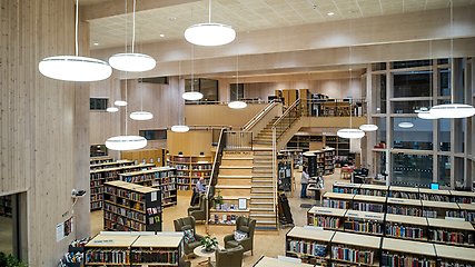 Överblick över biblioteket. Rader med bokhyllor fyllda med böcker och en stor trappa som leder upp till andra våningen.