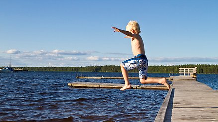 Pojke hoppar från en brygga ut i vattnet.