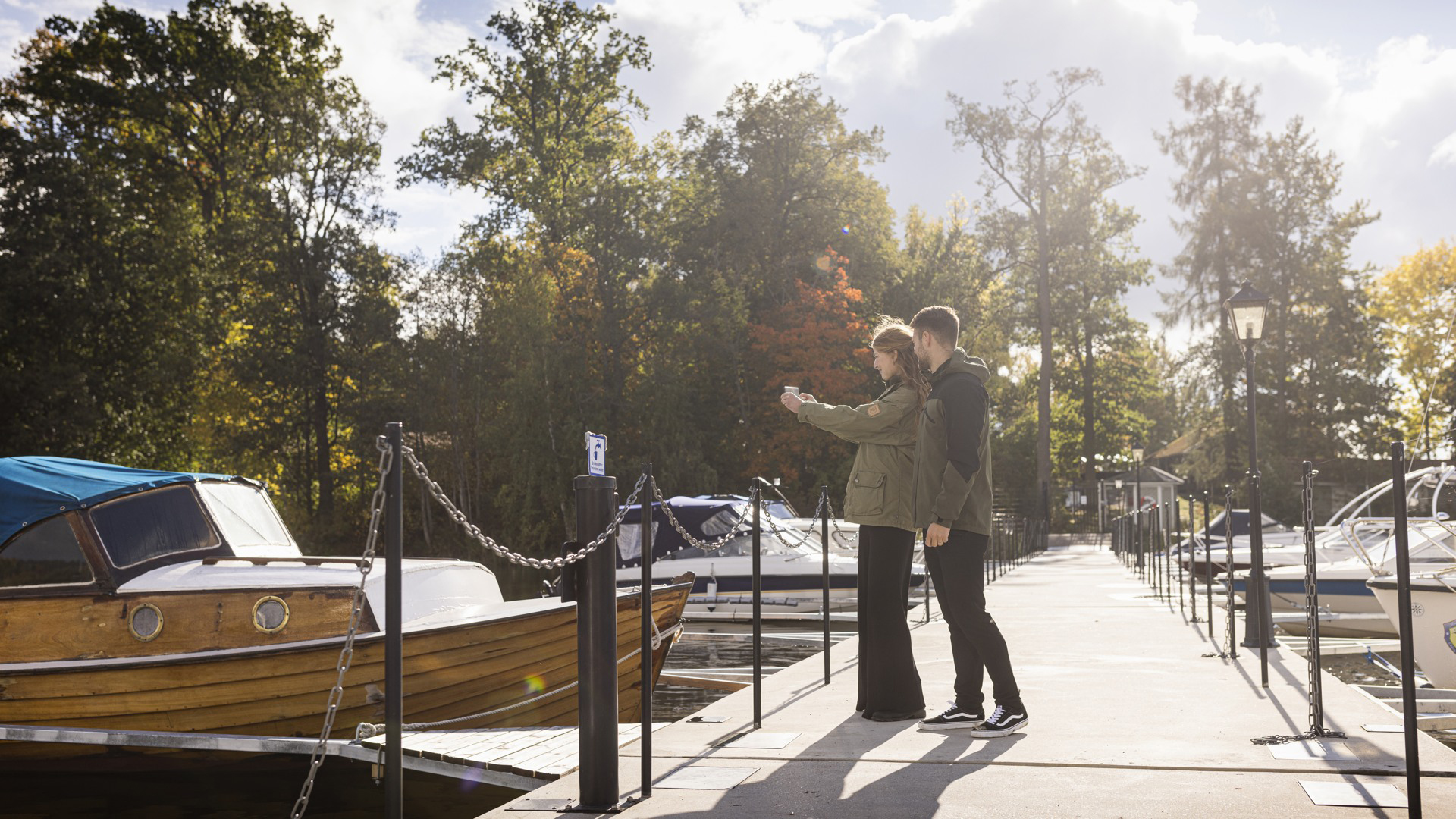 Två personer fotograferar en träbåt som ligger förtöjd vid gångbron till Borgmästareholmen