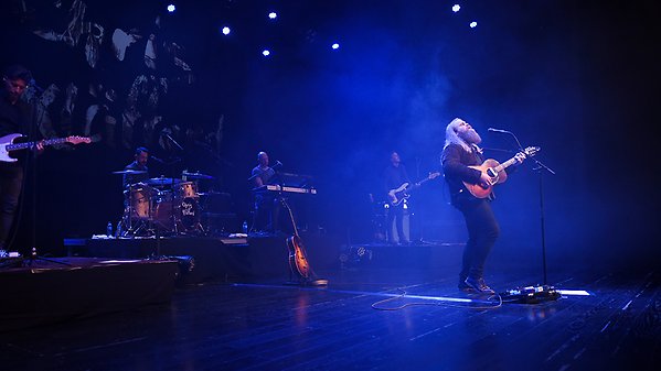 Chris Kläfford står på scenen i stora salongen och sjunger och spelar gitarr. Han har sitt band bakom sig och de står i ett blått ljus.