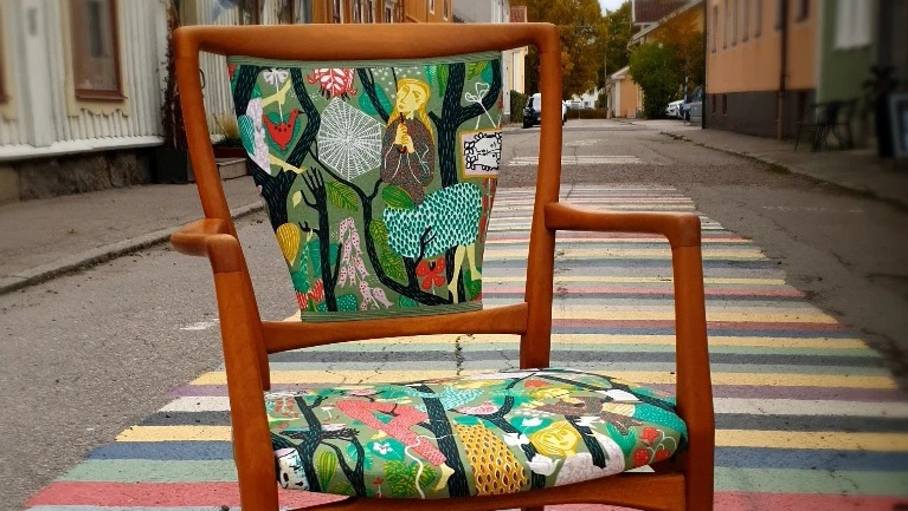 Karmstol med mönstrad tyg står mitt på en gata. En målad trasmatta syns på gatan under stolen.