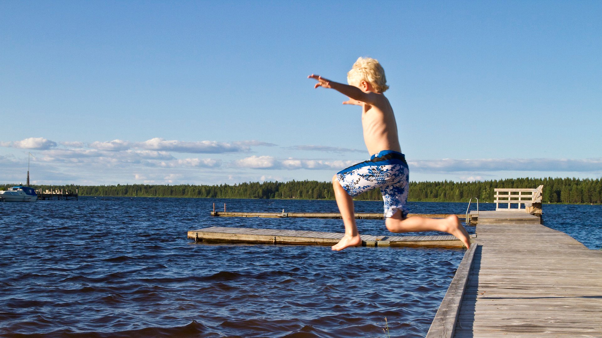 Pojke hoppar från en brygga ut i vattnet.