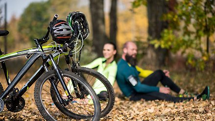Två cyklister sitter vid kanten av cykelvägen i skogen med sina cyklar framför sig.