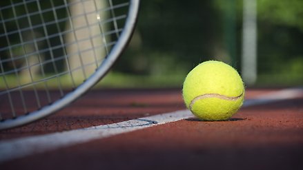 närbild på tennisboll på hårdgjord yta med markerad linje samt del av tennisrack
