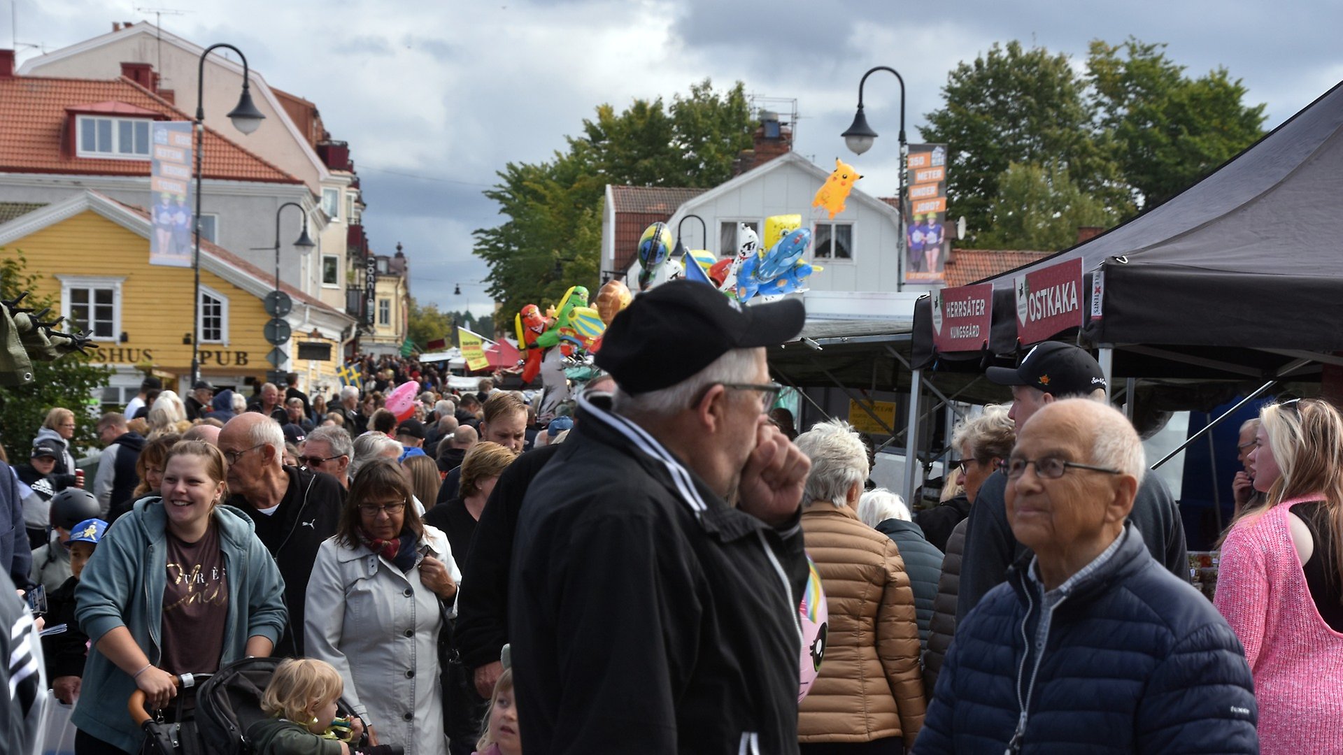 Genomfartsgatan i Askersund fylld med människor och marknadsstånd. Två äldre män i förgrunden som pratar med varandra.