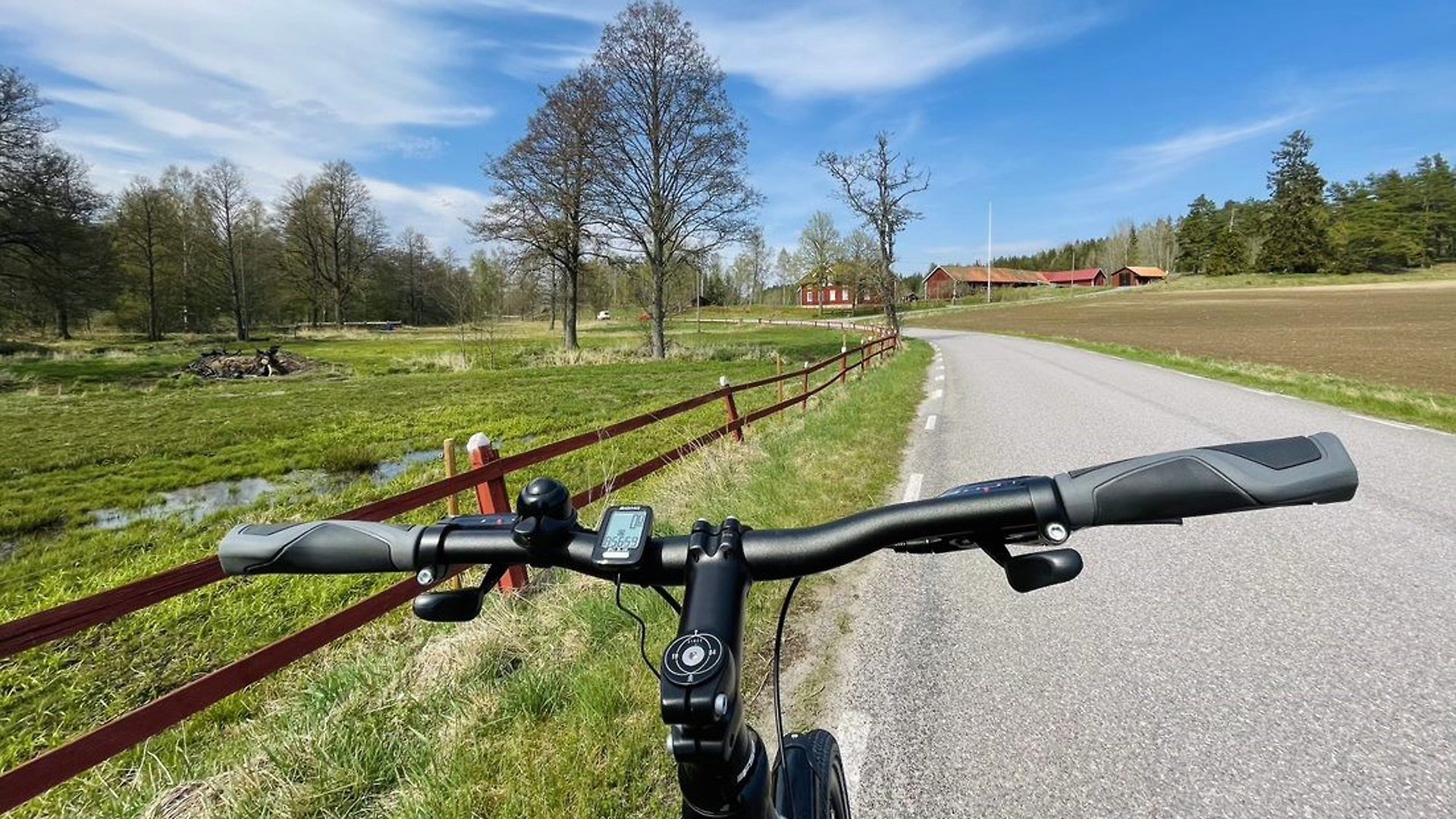 Cykelstyre. landsväg och hage med staket på ena sidan och åker på andra sidan. 