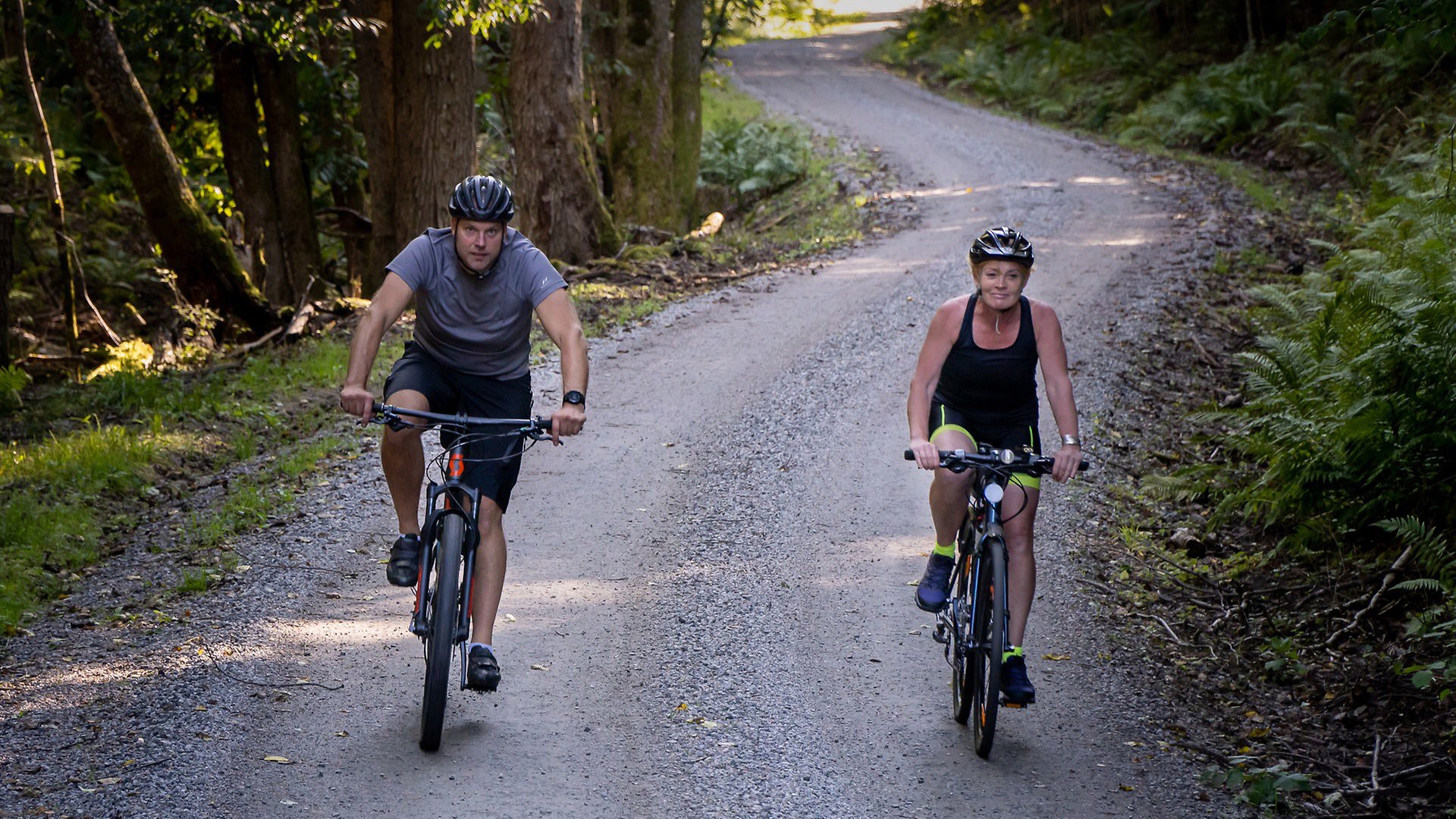 Två cyklister som cyklar på en grusväg i skogen.