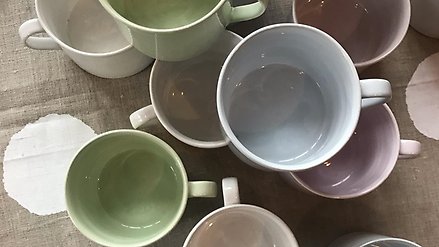 Koppar i olika färger står staplade på varandra på ett bord.