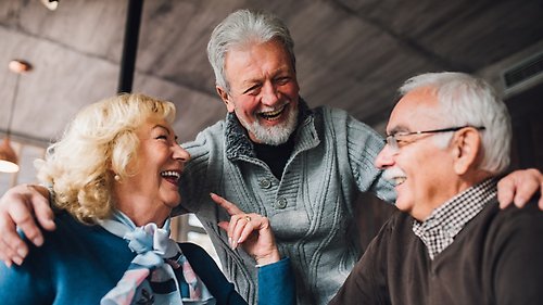 två äldre herrar och en dam är i ett trevligt samtal, skrattar och håller om varandra.