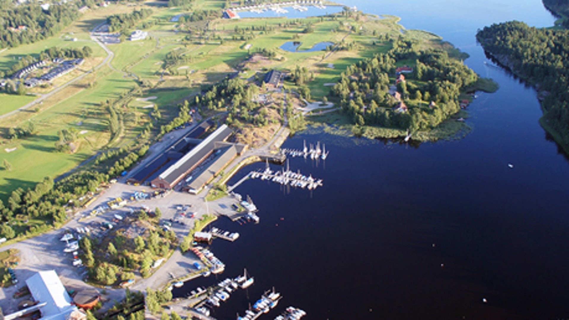Drönarfoto taget uppifrån på Åmmebergs hamn. Vattendrag, flera bryggor med båtar, stora grönområden och flera byggnader finns. 