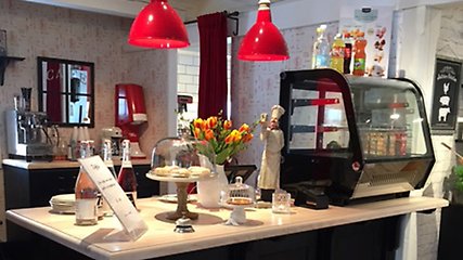 Cafédisk med olika bakverk och drycker samt en vas med orangea tulpaner. Över disken hänger två röda lampor. 