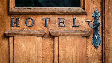 Trädörr med texten "hotel" i svarta bokstäver. Ett handtag i svart metall finns till höger av bilden. 