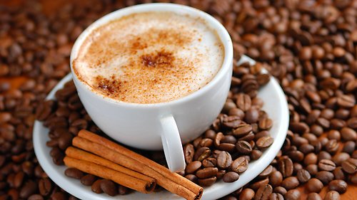 Cappuccino i en kaffekopp med fat stående på en massa kaffebönor.