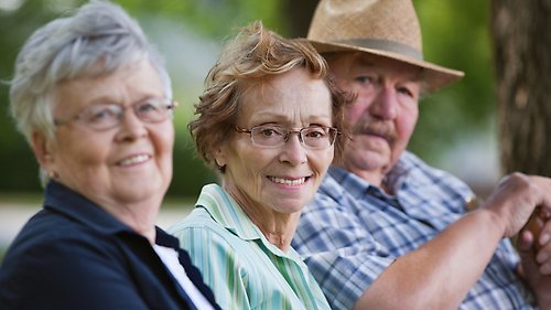 Tre äldre personer som sitter tillsammans med natur i bakgrunden.
