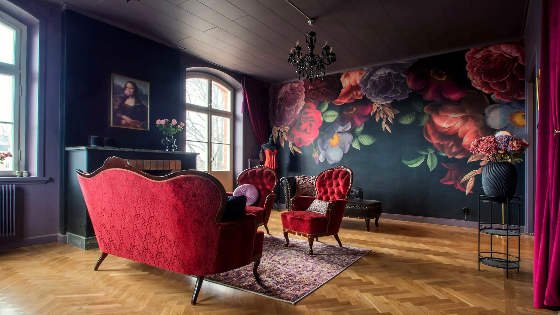 Röd soffa och fåtölj i rum med stora fönster och storblommiga tapeter.