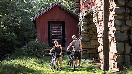 Två cyklister som utforskar en gammal byggnad och skog i bakgrunden.