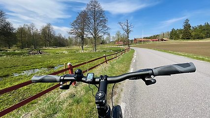 Cykelstyre. landsväg och hage med staket på ena sidan och åker på andra sidan. 