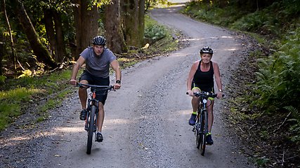 Två cyklister som cyklar på en grusväg i skogen.
